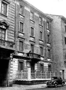 Foto in bianco e nero della facciata dell'ingresso di Working Milano negli anni '50. Per strada una macchina d'epoca.